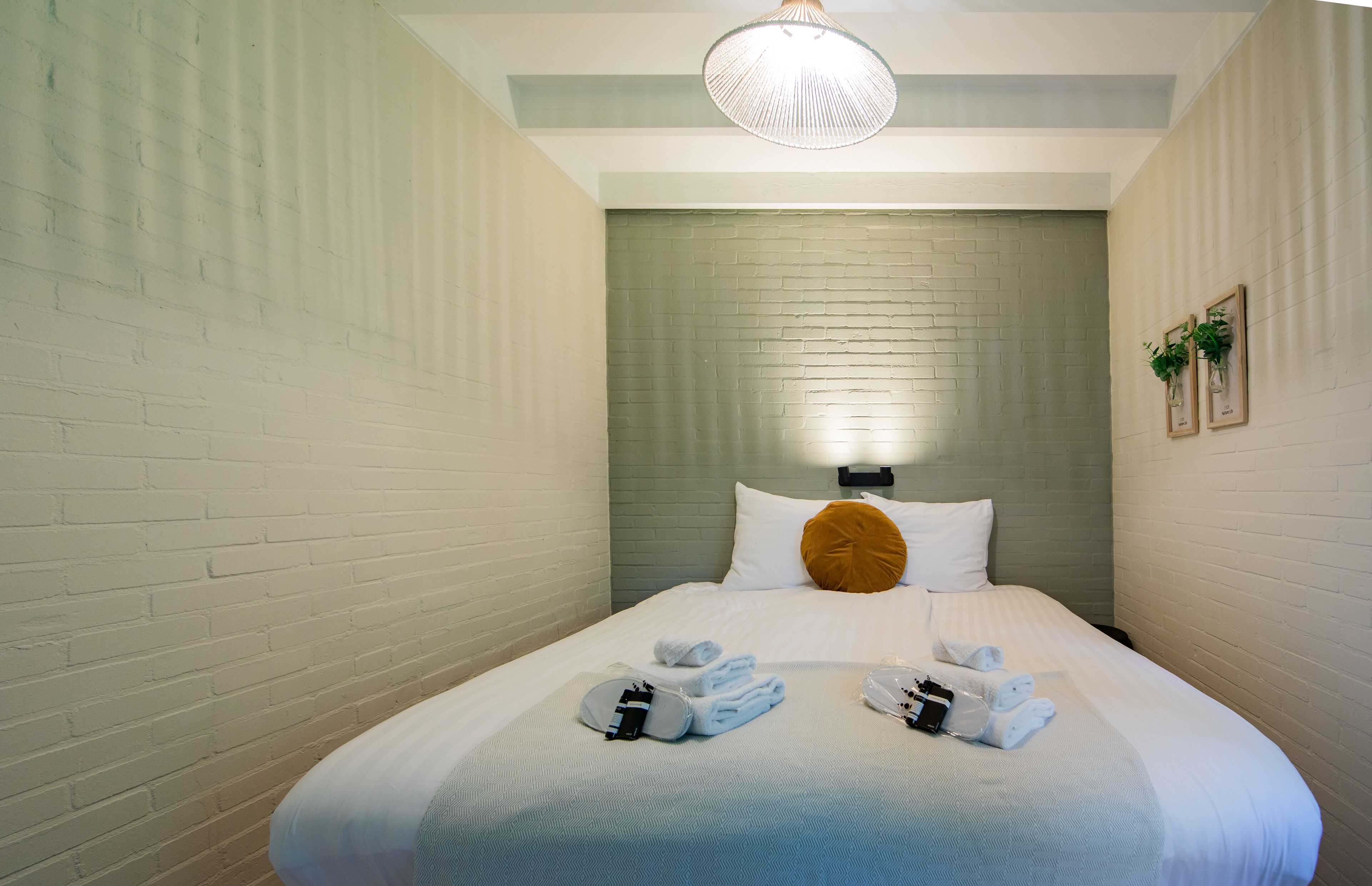 A hotel room with a neatly made bed, a headboard, and a wall-mounted light fixture.