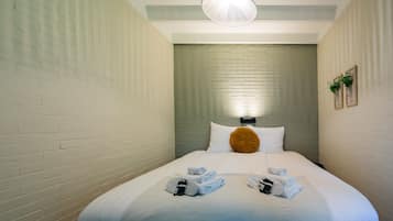 A hotel room with a neatly made bed, a headboard, and a wall-mounted light fixture.