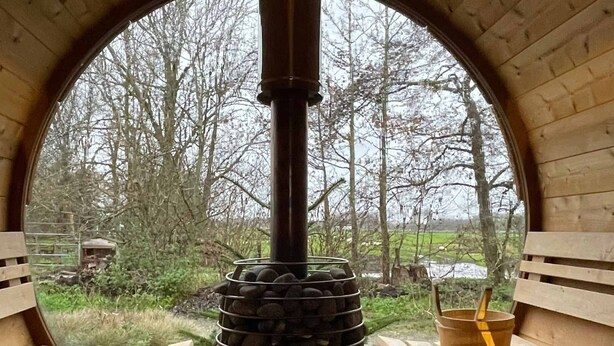 Un horno de piedra en una estructura de madera con bancos y vistas a árboles y un campo.