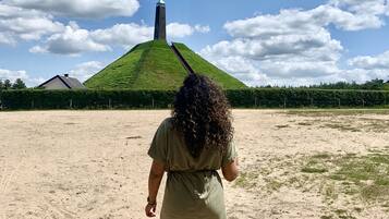 Eine Person geht auf einem sandigen Pfad auf einen grünen Hügel zu, auf dem ein Turm steht.