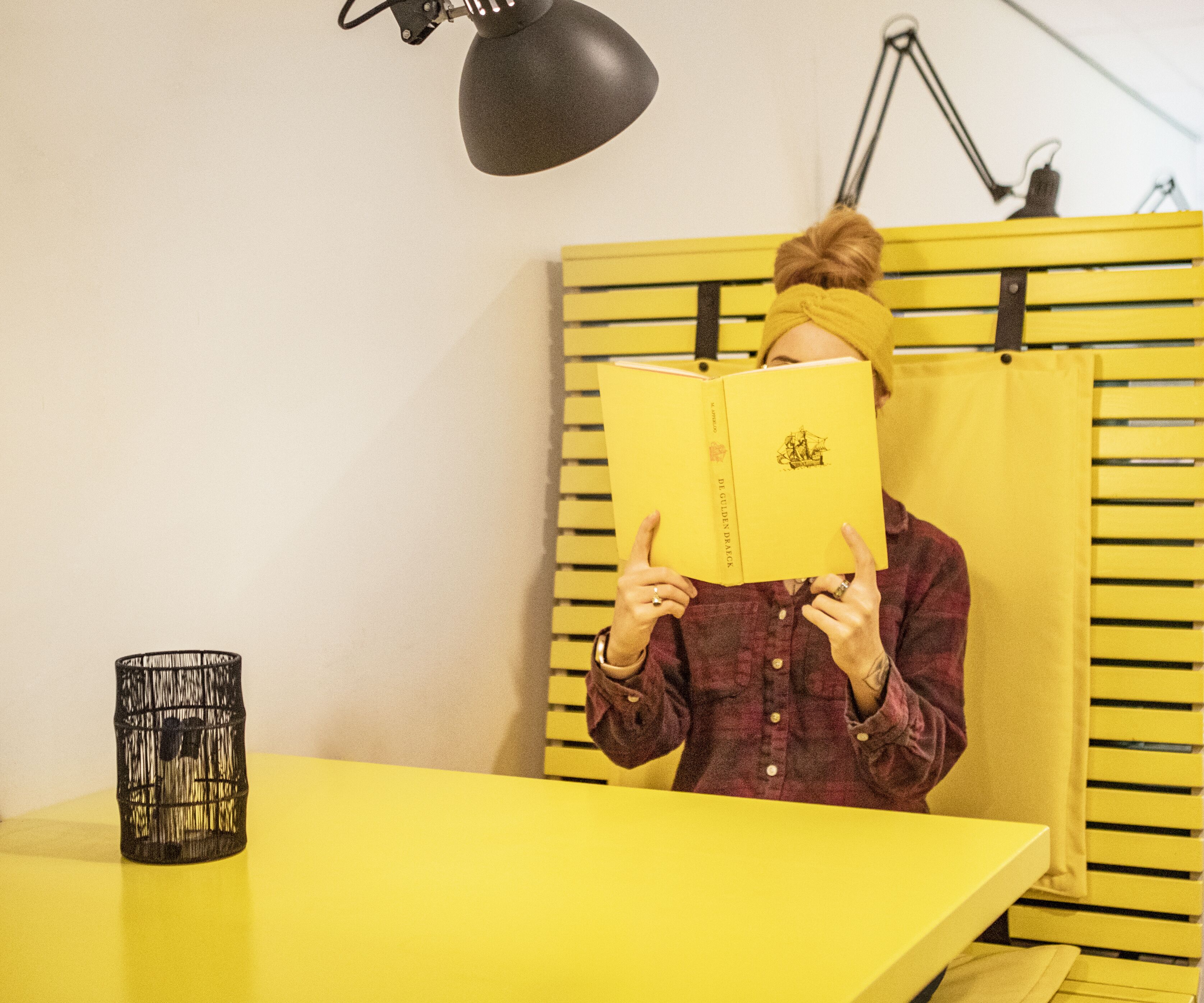 Una persona leyendo un libro en una habitación con paredes y una mesa amarillas.