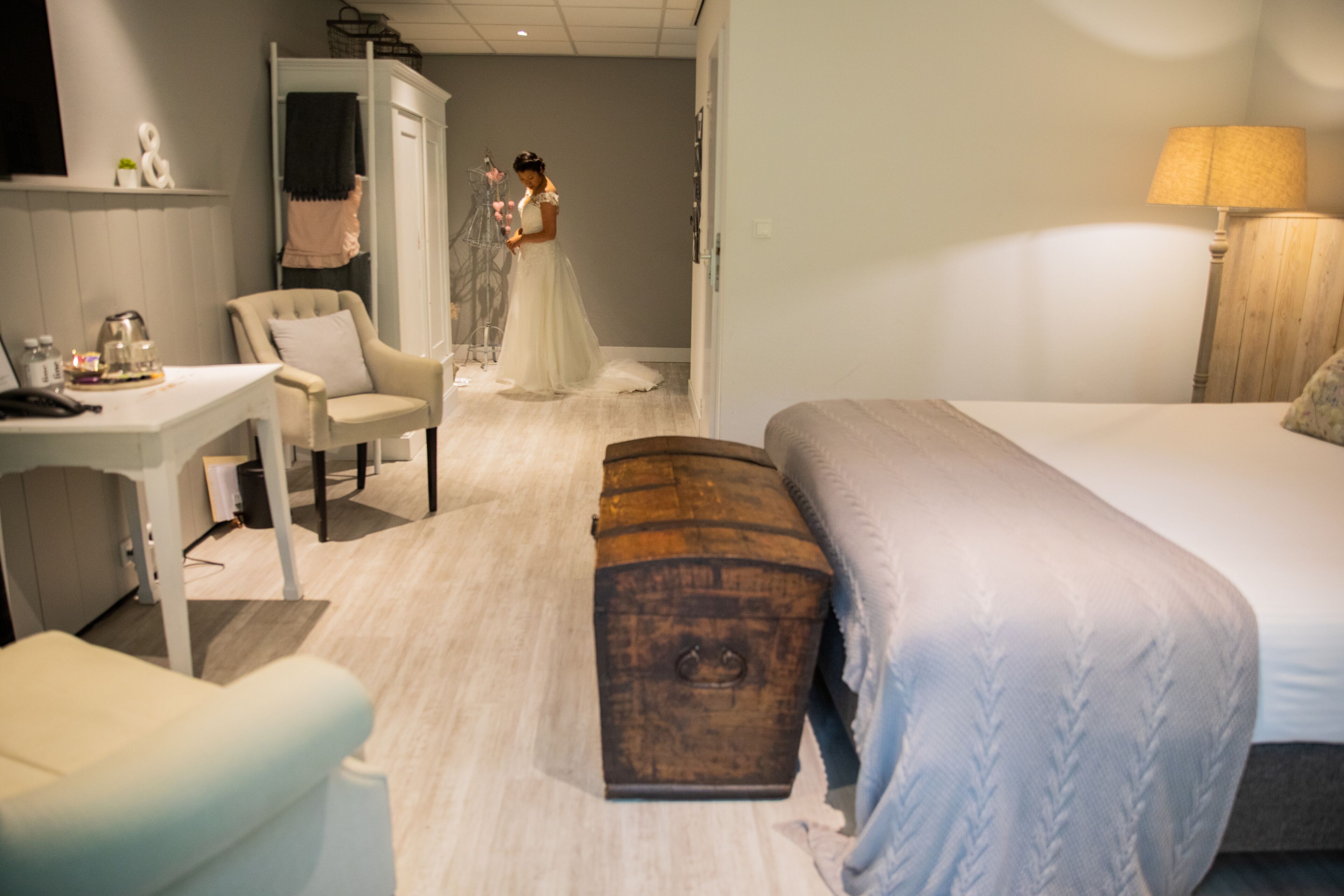 Una habitación de hotel con cama, escritorio, silla, armario y un banco.