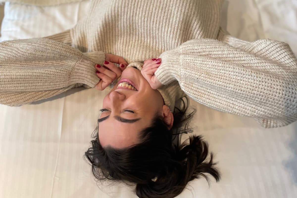 A person lying on a bed with a white blanket and a patterned pillow.