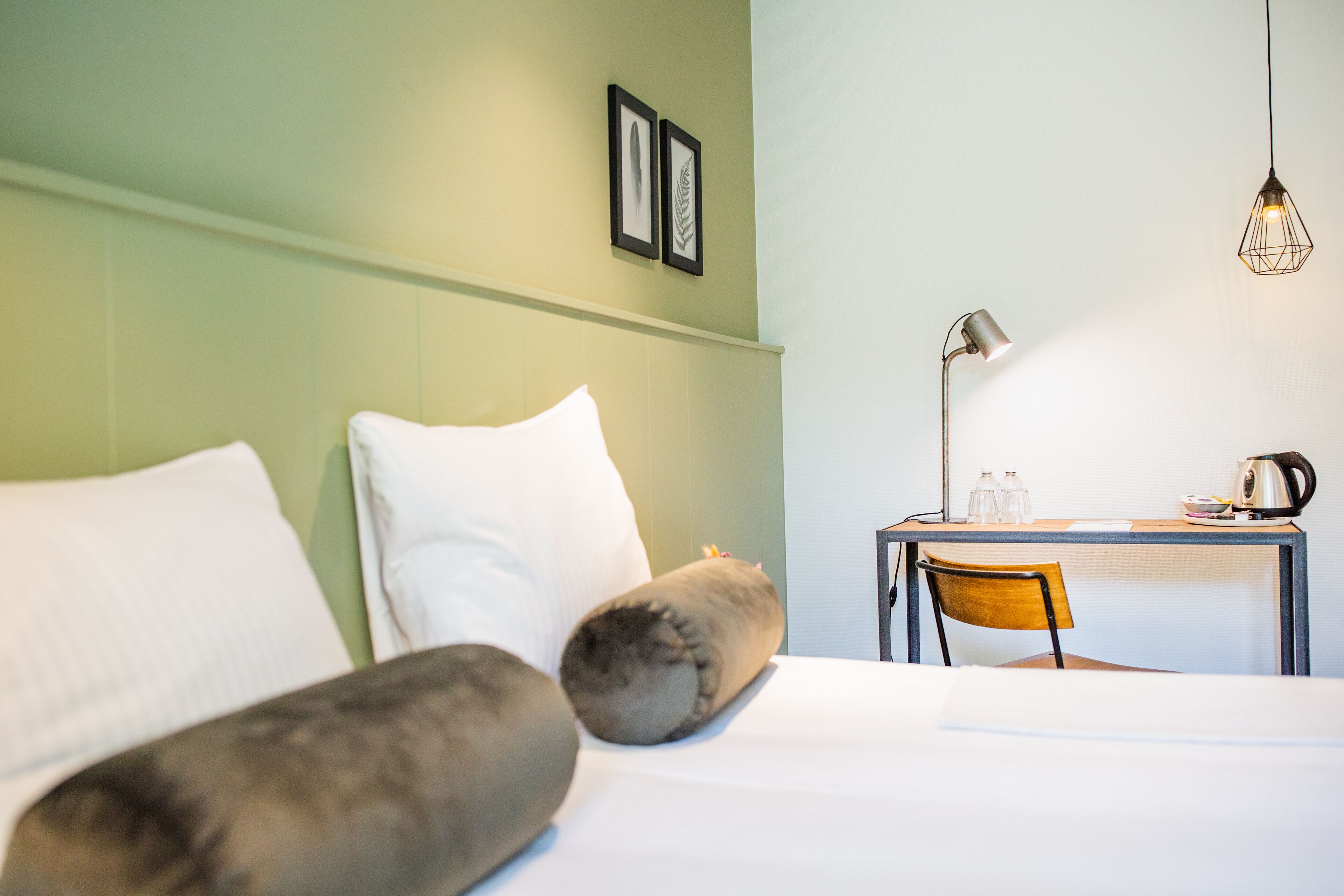 Une chambre d’hôtel comprenant un lit, des oreillers, un bureau avec une chaise, une lampe et un luminaire suspendu.