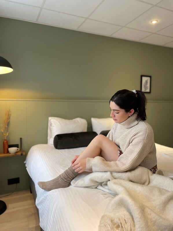 A person sitting on a bed in a room with a green wall, a white ceiling, and a framed picture on the wall. - Buitenplaats de Bergse Bossen (Driebergen)
