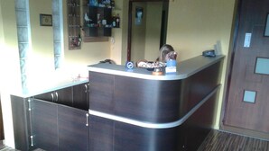A reception desk with a dark wood finish and a curved design. There is a small shelf above the desk with various items, including a box labeled "Lunchies." The room has a wooden floor and a door with a panel design. - Willa Mewa (Gdynia)