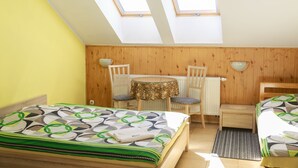 A bedroom with a skylight, a bed with a patterned bedspread, a small table with a decorative tablecloth, two chairs, and a wooden nightstand. - Willa Mewa (Gdynia)