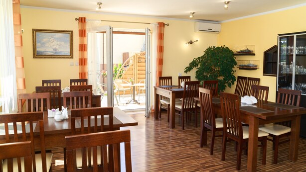 A dining area with wooden tables and chairs, a staircase leading to an outdoor area, and a large potted plant. - Willa Mewa (Gdynia)