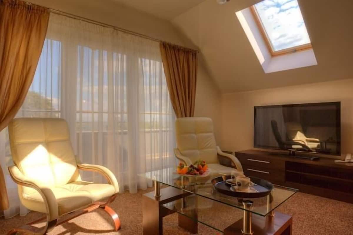 A hotel room with a large window, a sofa, a glass coffee table, a TV, and a desk with a lamp.