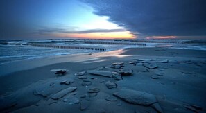A beach with scattered rocks and a wooden breakwater. - Hotel 77 Restauracja Spa (Wladyslawowo)