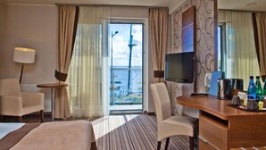 A hotel room with a bed, a desk, a chair, a television, and a view of the sea through a large window. - Hotel 77 Restauracja Spa (Wladyslawowo)