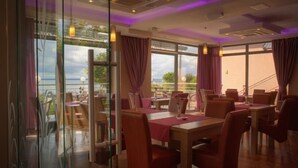 A restaurant with tables and chairs, large windows with curtains, and a view of the outdoors. - Hotel 77 Restauracja Spa (Wladyslawowo)