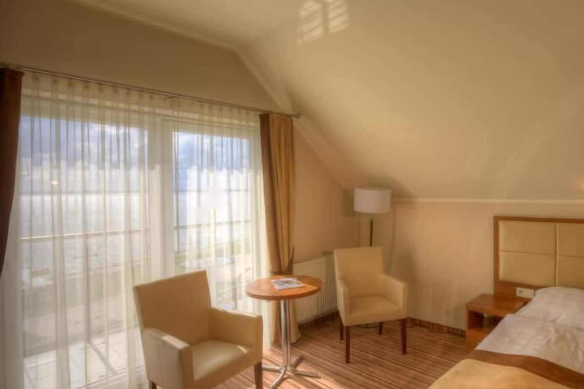 A hotel room with a bed, a chair, a small table, and a lamp.