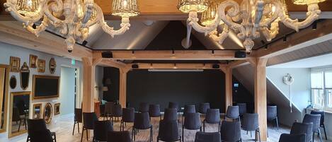 A spacious room with a stage, black chairs, and ornate chandeliers.