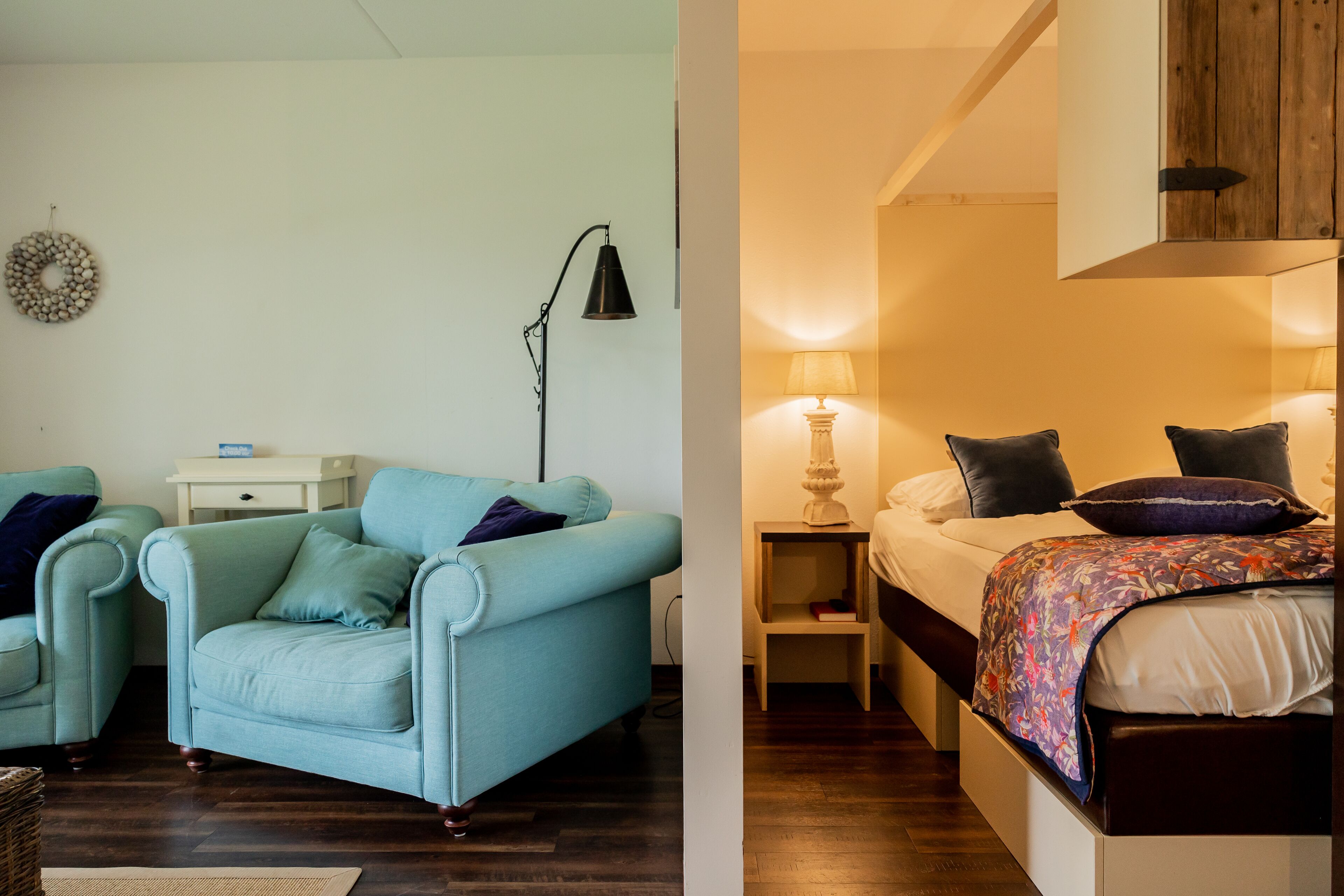 A room with a light blue armchair, a bedside table with a lamp, and a bed with a floral bedspread.