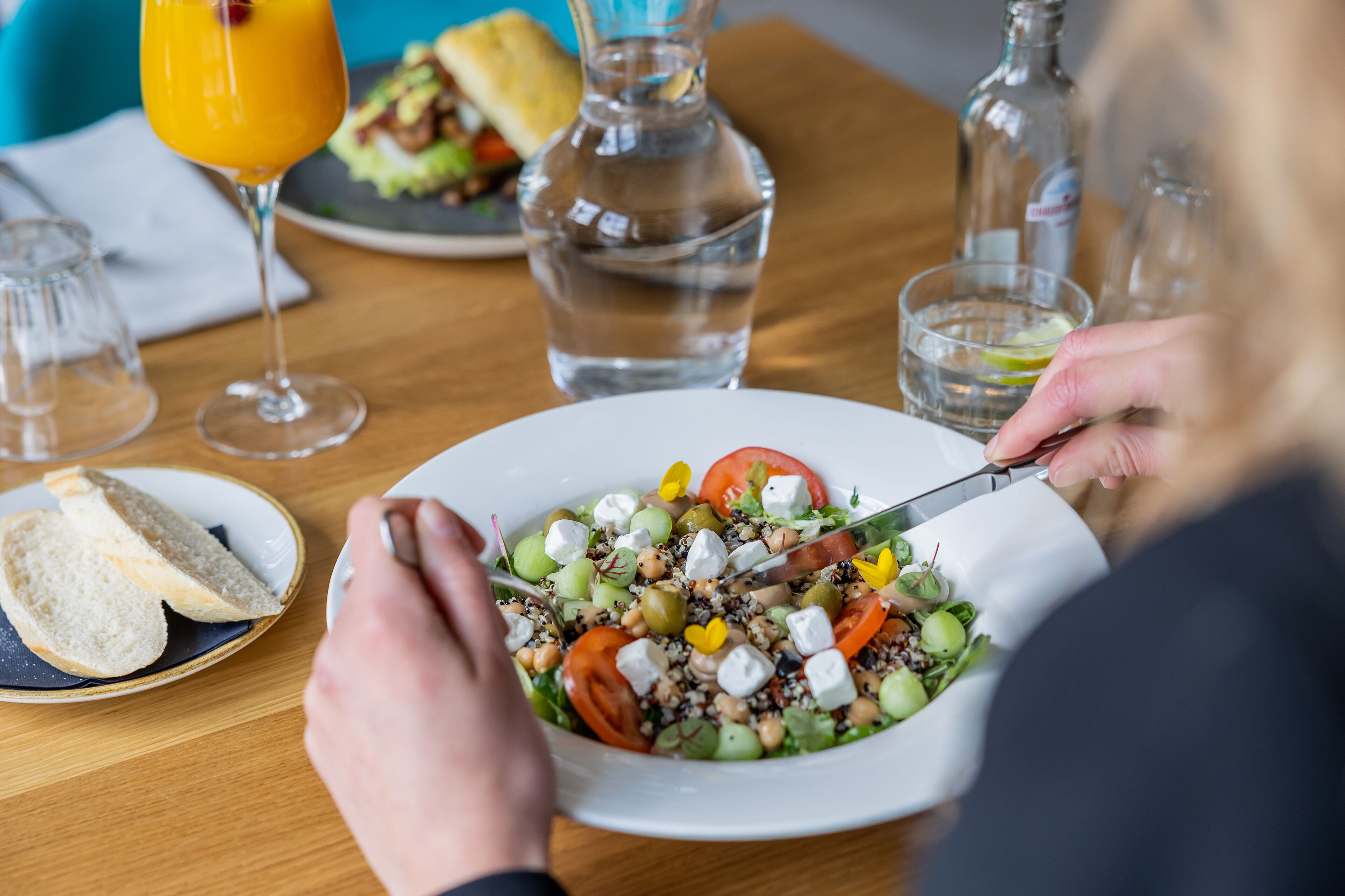 A dining table with a plate of salad, a glass of orange juice, and a bottle of water.