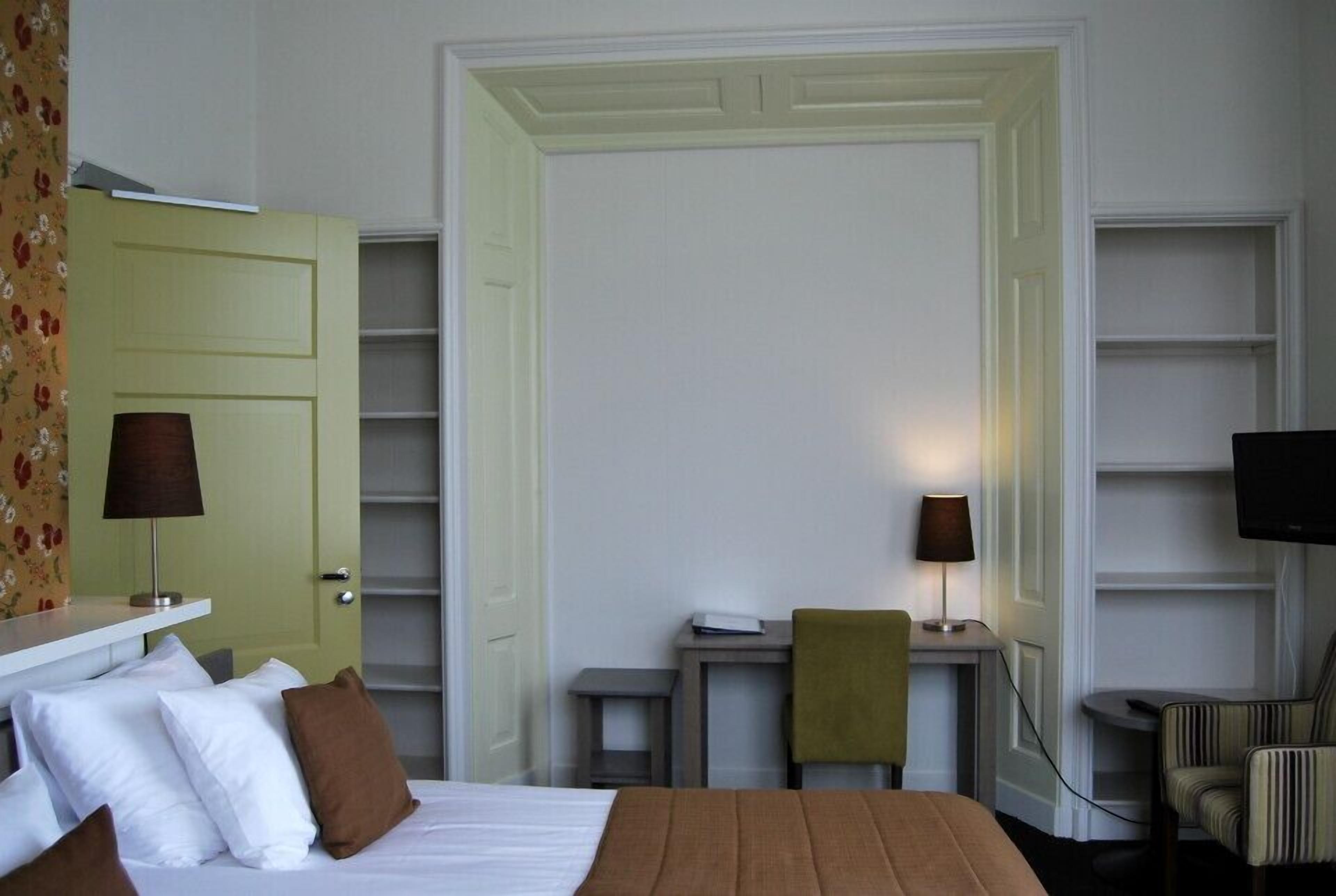 A hotel room with a bed, a desk, a chair, a television, and a wardrobe.