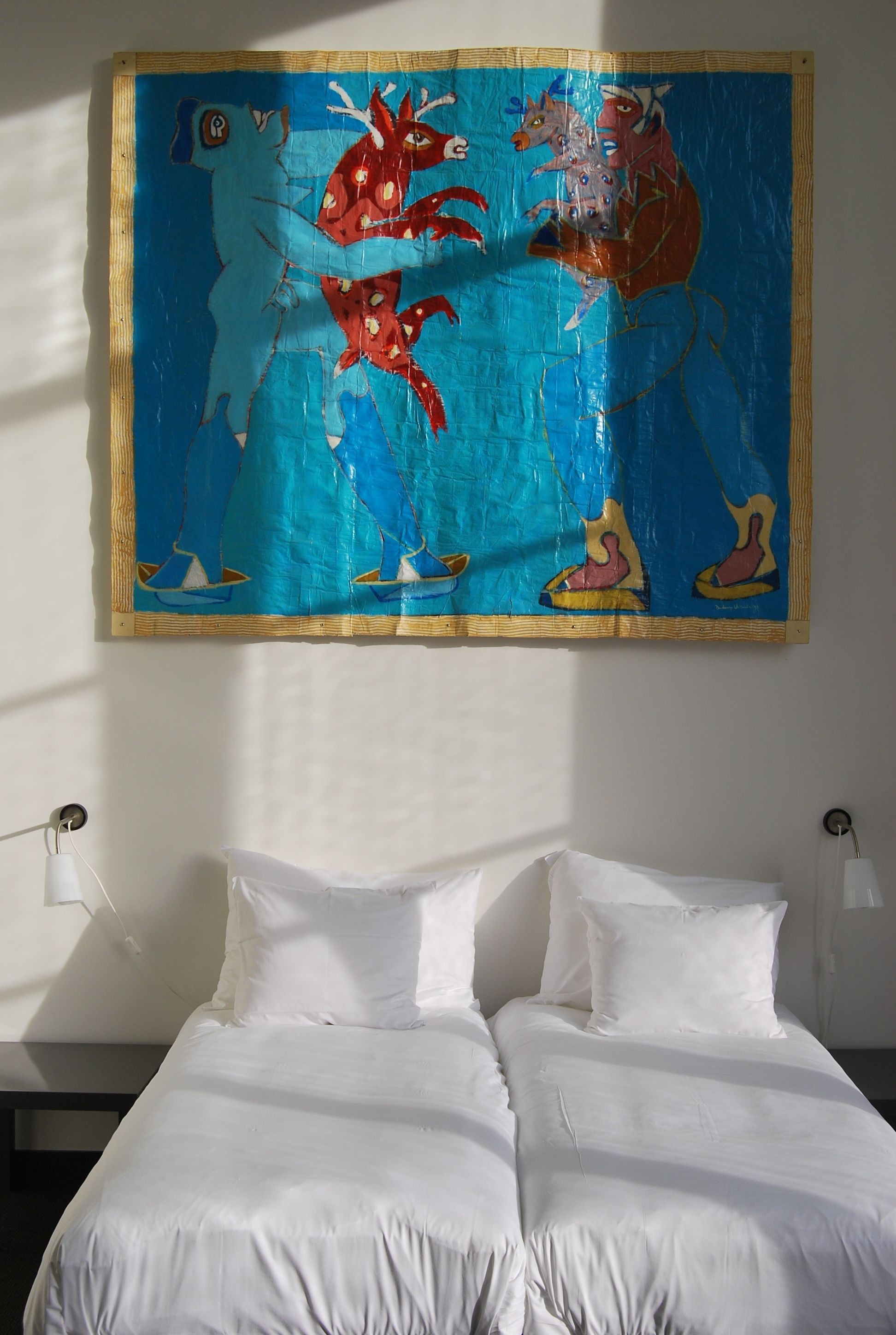 Una cama con sábanas blancas y un cuadro abstracto de colores sobre ella.