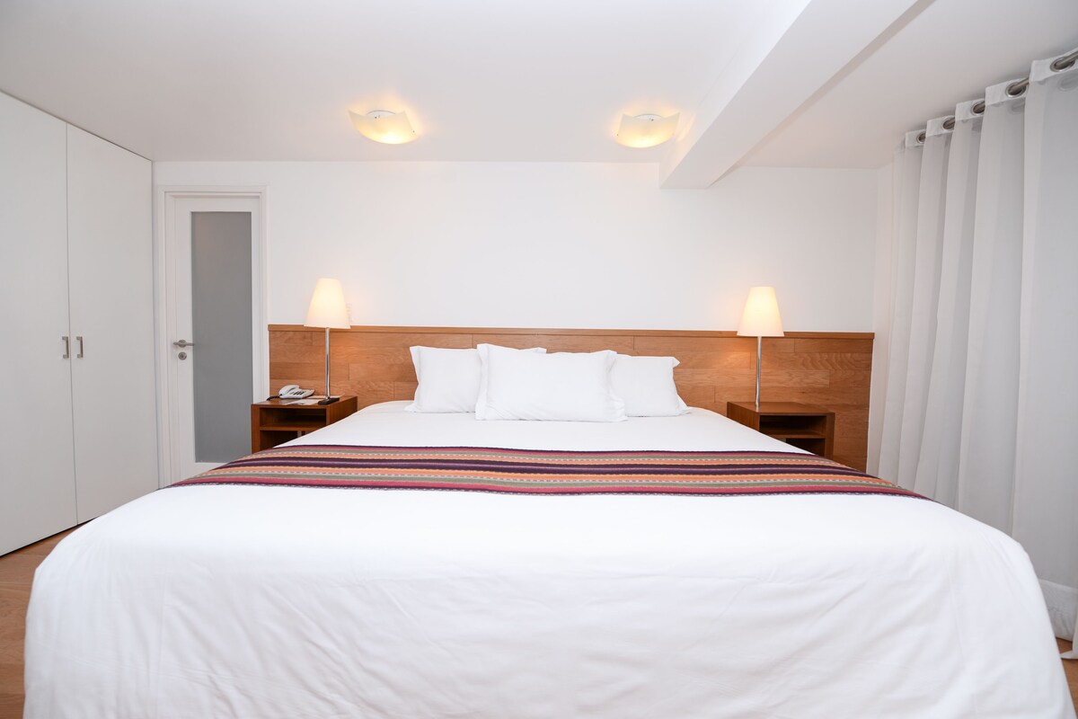 Una habitación de hotel con una cama grande, dos lámparas de noche, un cabecero de madera y una puerta.