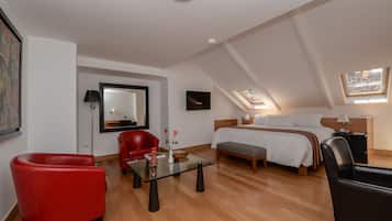 Una habitación de hotel moderna con una cama en altillo, un sillón rojo, una mesa de centro de vidrio y un amplio ventanal con vistas a la ciudad.