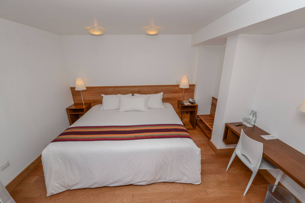 Una habitación de hotel con una cama grande, cabecera de madera, mesitas de noche, un escritorio y una silla.