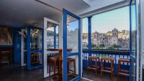 Ein Zimmer mit großem Fenster, Holzschemeln und Blick auf ein historisches Gebäude.