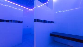 A modern bathroom with white walls, a black bench, and blue lighting.