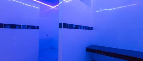 A modern bathroom with white walls, a black bench, and blue lighting.