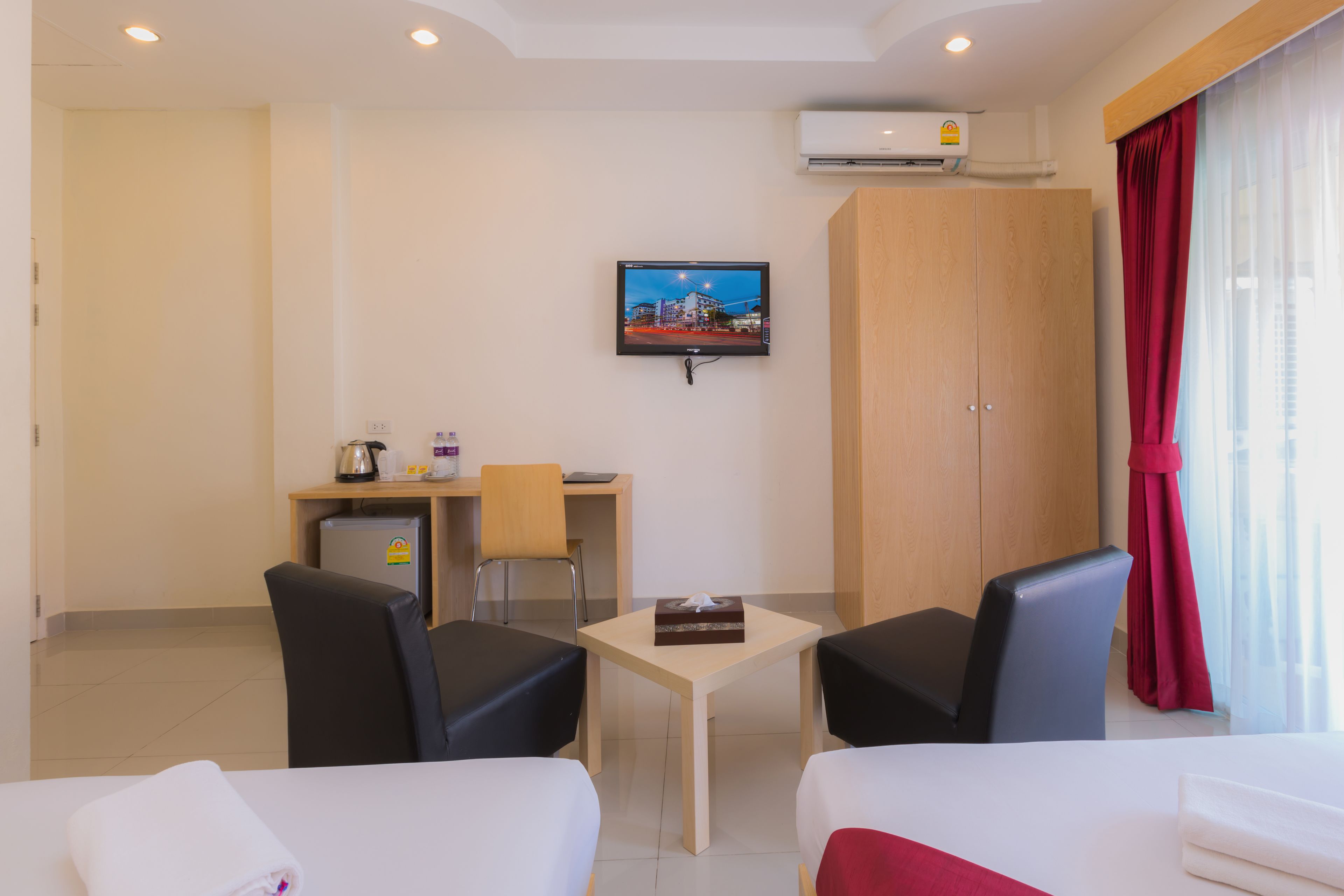Habitación de hotel con dos camas, un escritorio con silla, un televisor montado en la pared y un equipo de aire acondicionado sobre el escritorio.