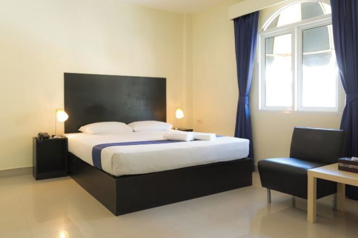 A neatly arranged hotel room with a large bed, bedside lamps, a small table, and a window with curtains.