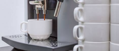 Una cafetera con una taza y una pila de tazas blancas.