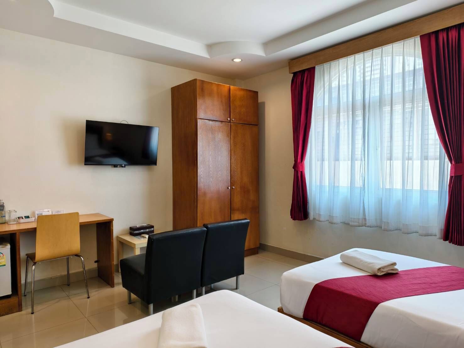 Une chambre d’hôtel avec deux lits, une télévision, un bureau avec une chaise et une armoire.