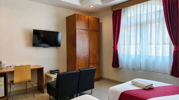 Une chambre d’hôtel avec deux lits, une télévision, un bureau avec une chaise et une armoire.