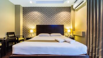 Une chambre d’hôtel avec un grand lit, deux tables de chevet avec des lampes, un bureau avec une chaise et un papier peint à motifs.