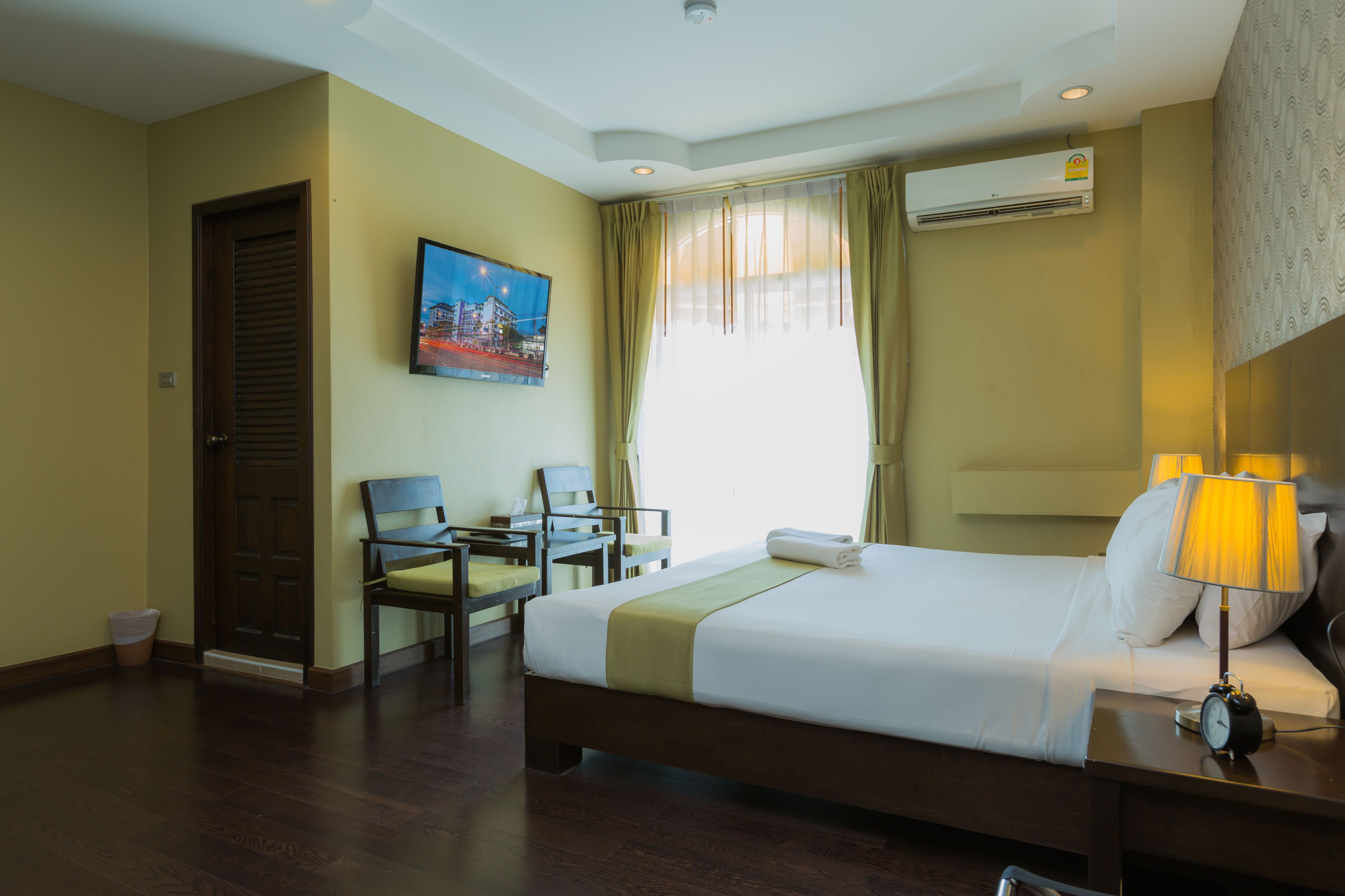 A hotel room with a bed, a desk, a chair, a TV, and an air conditioning unit.