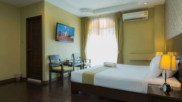 A hotel room with a bed, a desk, a chair, a TV, and an air conditioning unit.