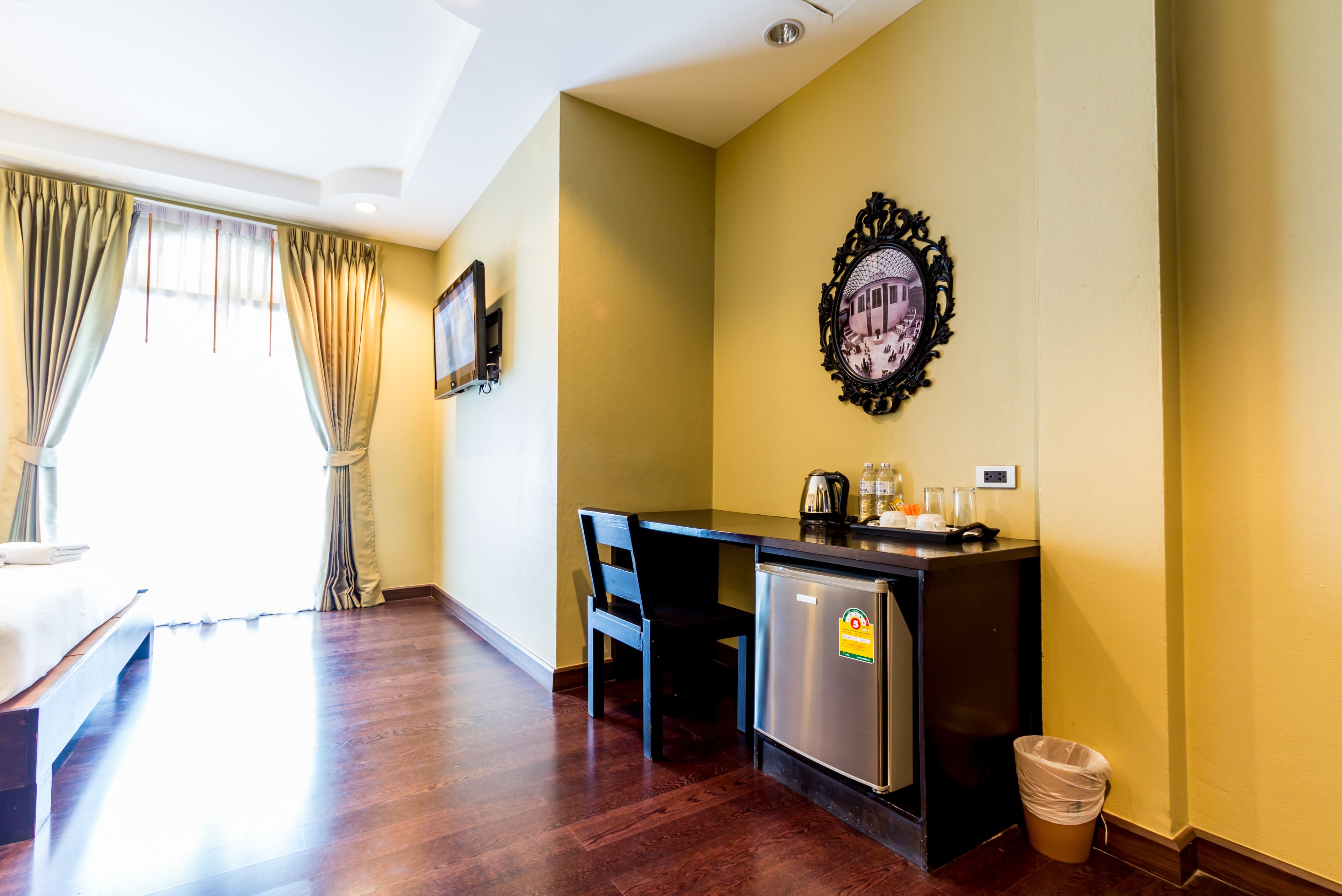 A compact room with a bed, a small kitchenette, a chair, and a trash bin.
