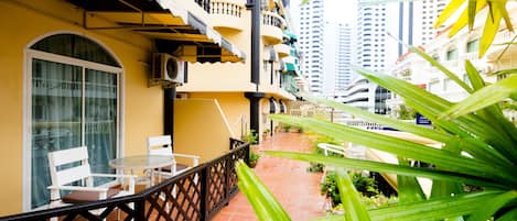 A balcony with a table and chairs, surrounded by potted plants and a view of tall buildings.