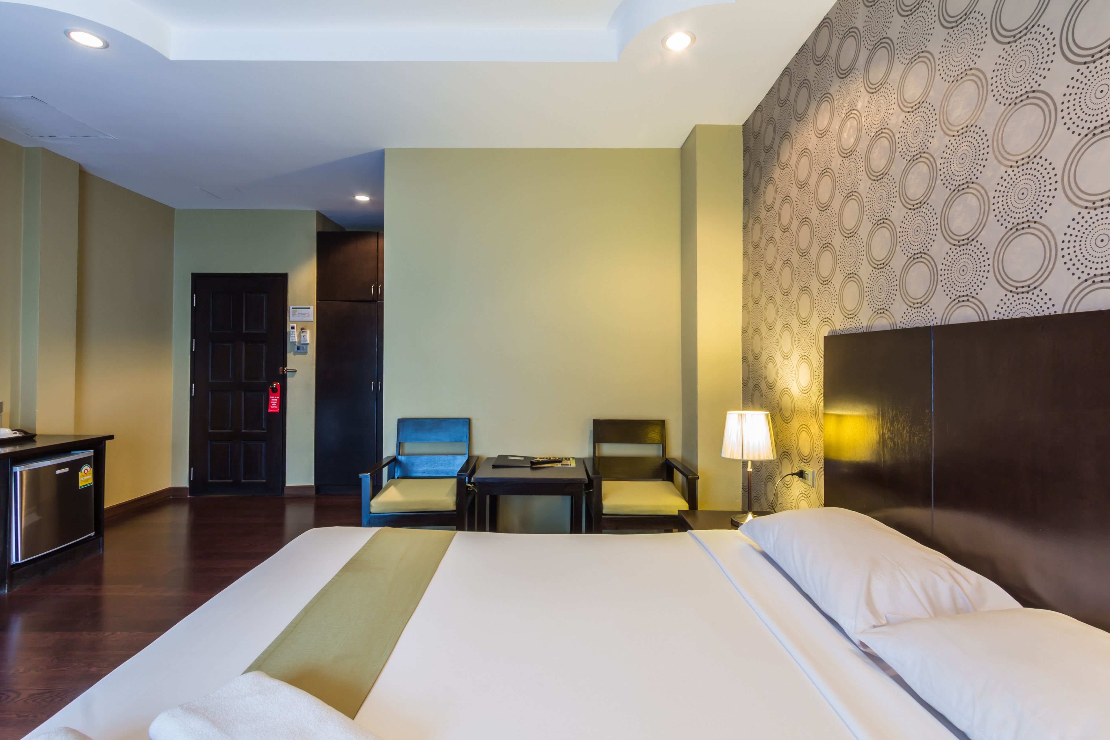 A hotel room with a large bed, two armchairs, a desk, and a wall-mounted lamp.