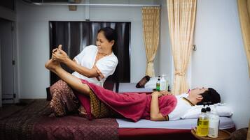 A massage therapy session in a room with a bed, massage table, and bottles of massage oil on a small table.