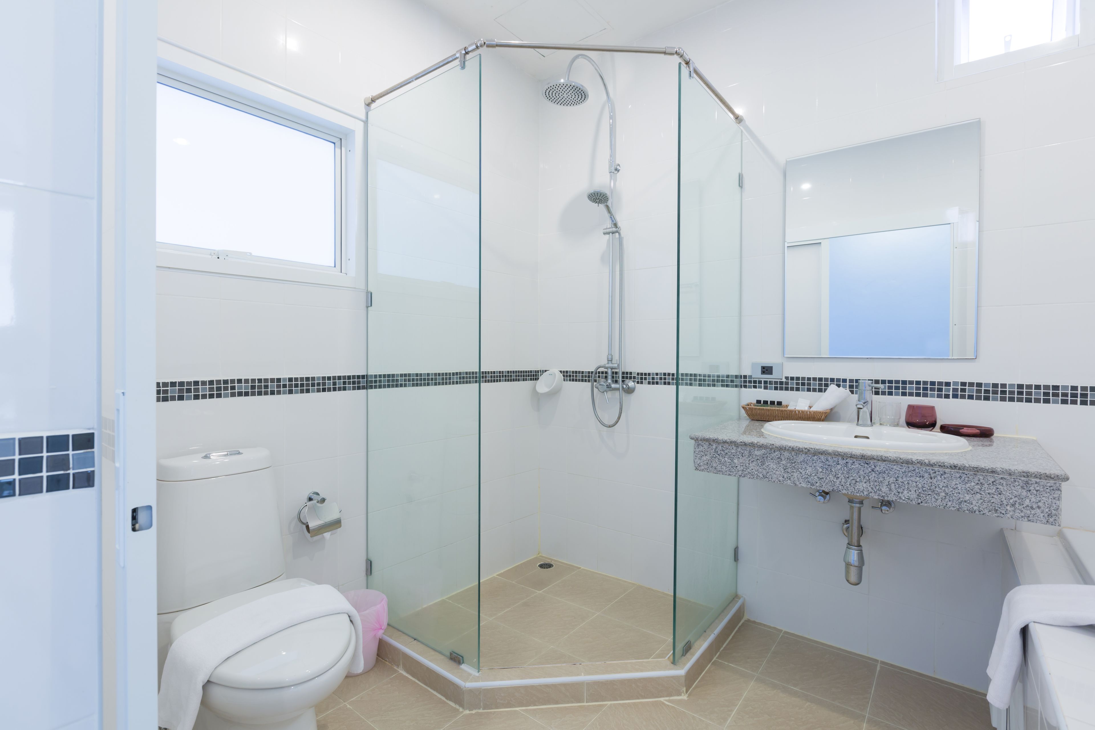 Une salle de bain moderne avec une douche à parois de verre, des toilettes blanches, un lavabo avec un miroir au-dessus et un sol carrelé.
