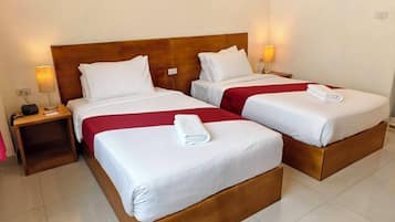 Dos camas individuales con cabeceros de madera, ropa de cama blanca y colchas rojas. Cada cama tiene una toalla blanca doblada en el reposapiés. Hay lámparas de noche y un teléfono en la mesita de noche al lado de cada cama.