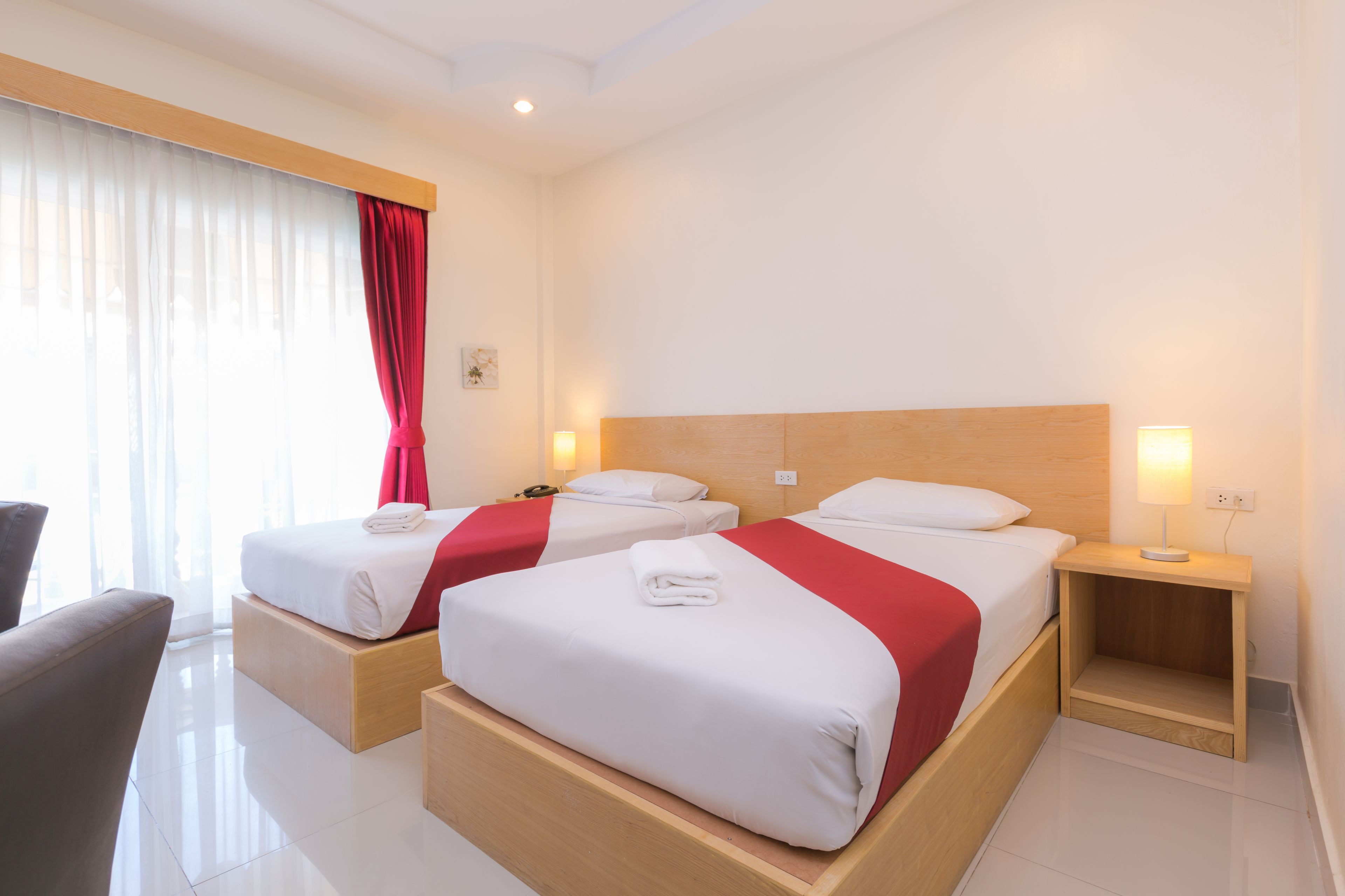 Een hotelkamer met twee bedden, een houten hoofdbord, een nachtkastje met een lamp en een stoel.