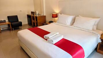 A hotel room with a large bed, a desk, a chair, and a nightstand with a lamp.