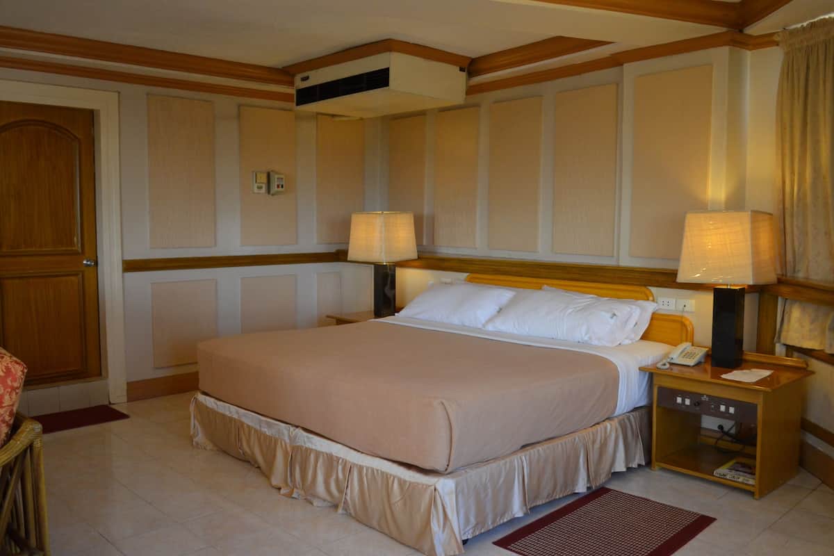 A hotel room with a large bed, two bedside tables with lamps, a wooden headboard, and a wooden door.