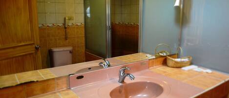Un baño con lavamanos rosa, un espejo y una zona de ducha.