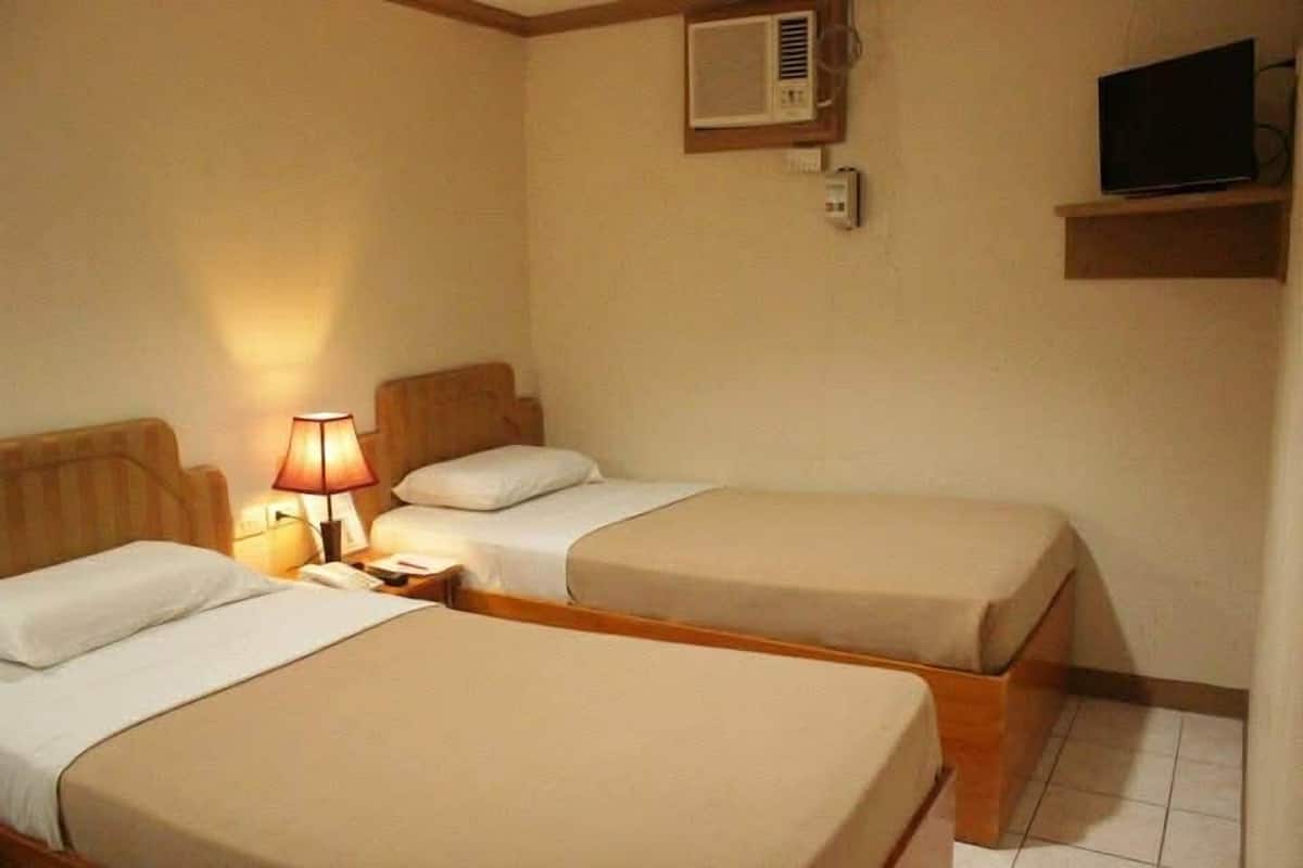 A hotel room with two beds, a bedside lamp, an air conditioning unit, and a television on a shelf.