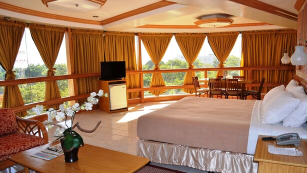 A hotel room with a bed, a desk, a TV, a dining area with chairs, and a balcony with curtains. - Elegant Circle Inn (Cebu City)