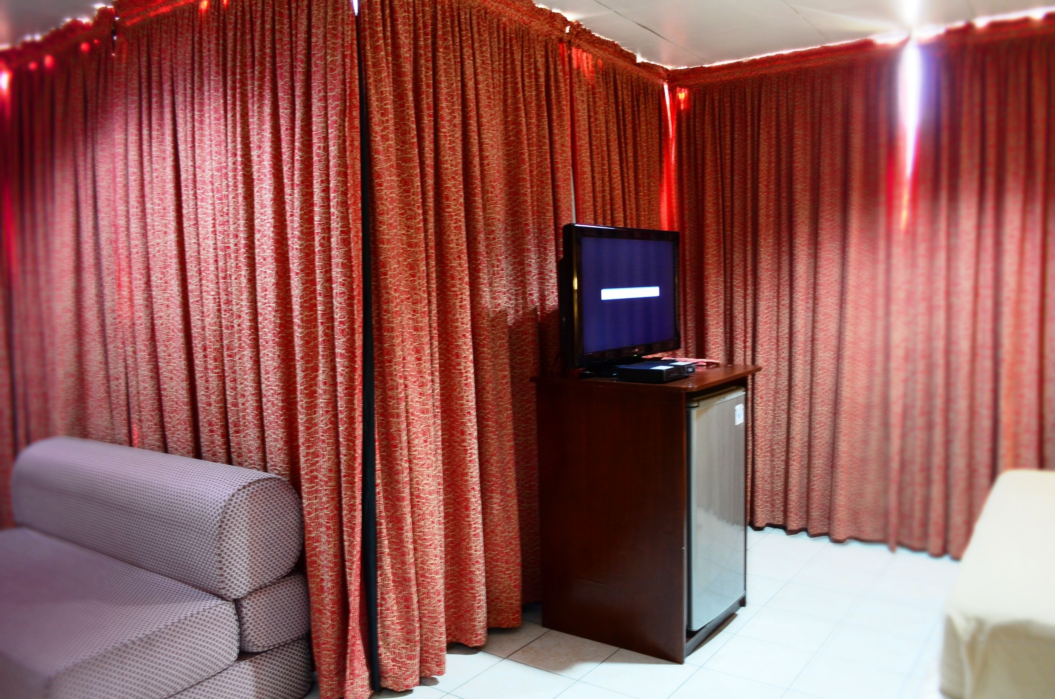 Una habitación con cortinas rojas, un televisor sobre un soporte de madera y un sofá.