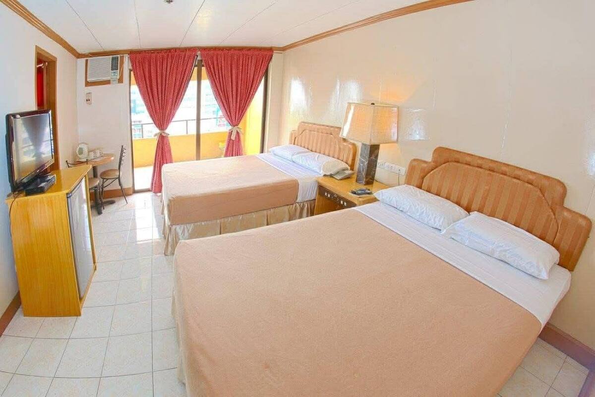 A hotel room with two beds, a TV, a desk with a chair, and a window with curtains.